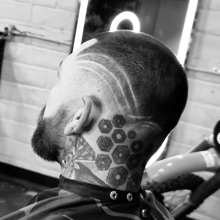 Skin fade with a shaved line detail through the side, blended into a tapered beard.